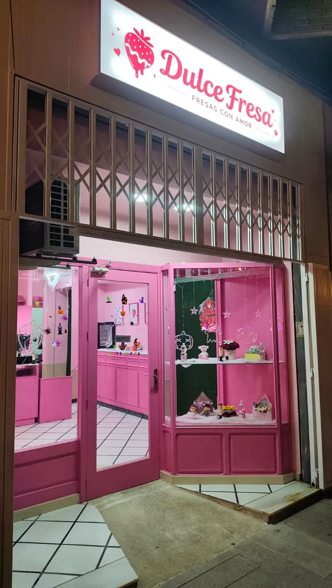 La fachada rosa de Dulce Fresa de noche con el rótulo iluminado